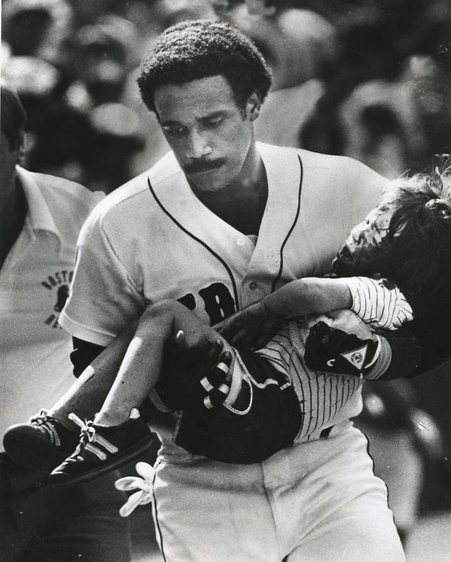 Jim Rice climbs into the Fenway Park stands from the dugout to assist a young boy who had just been hit in the head by a savage line drive foul off the bat of Dave Stapleton